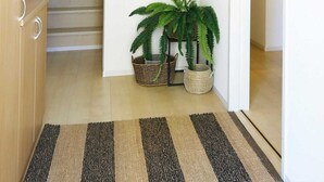 A hallway with a staircase, a wall-mounted light fixture, three woven wall decorations, a potted fern, and a striped rug. - Condomium Motobu Sakura Terrace (Motobu)