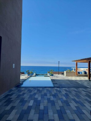 A swimming pool with a view of the ocean, a covered seating area, and a paved patio. - Beautiful apartment with a view of the sea (Tijuana)