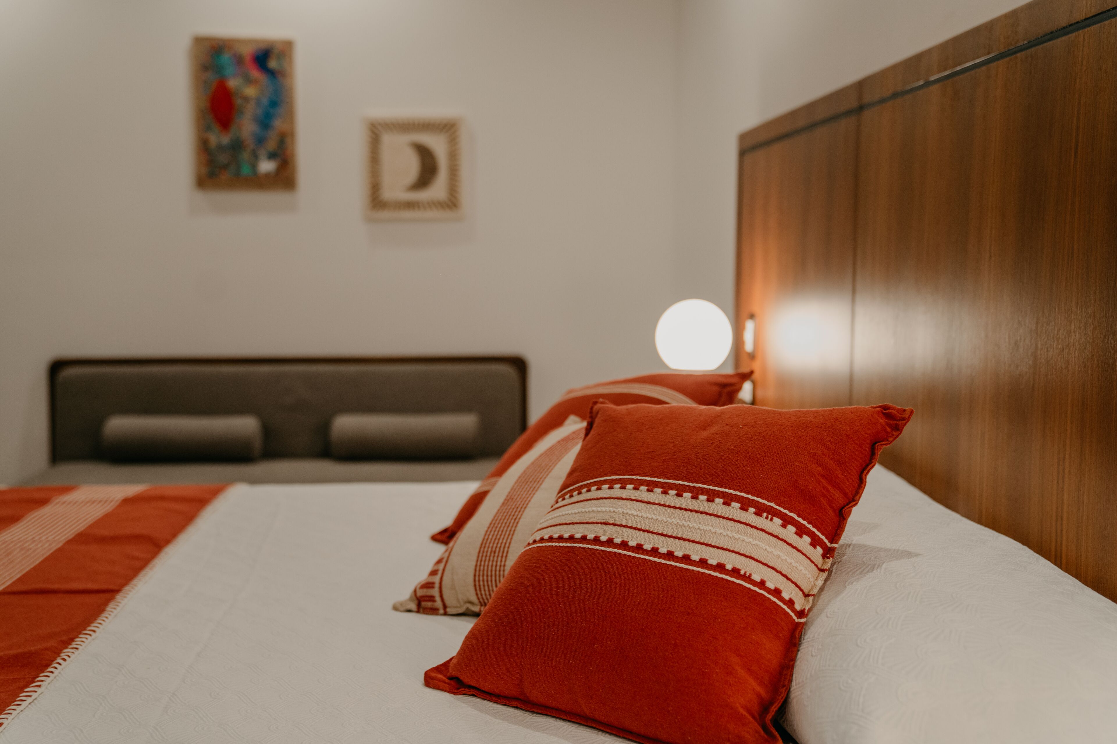 A neatly made bed with red and white pillows, a wooden headboard, and a bedside table with a round light.