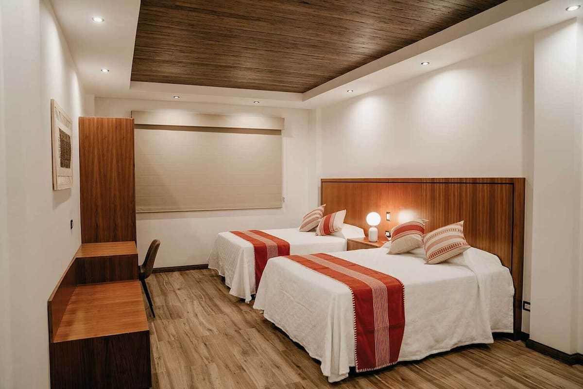 Ein Hotelzimmer mit zwei Betten, einem Holztisch, einem großen Fenster und einer Decke mit Einbuchtungslampen.