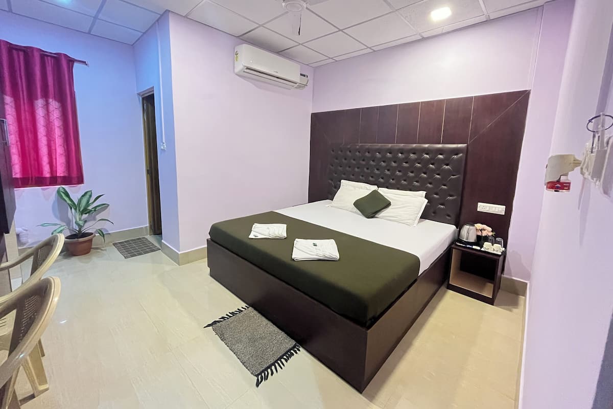 Ein Hotelzimmer mit Bett, Nachttisch, Blumentopf, Stuhl und einem Fenster mit Vorhängen.