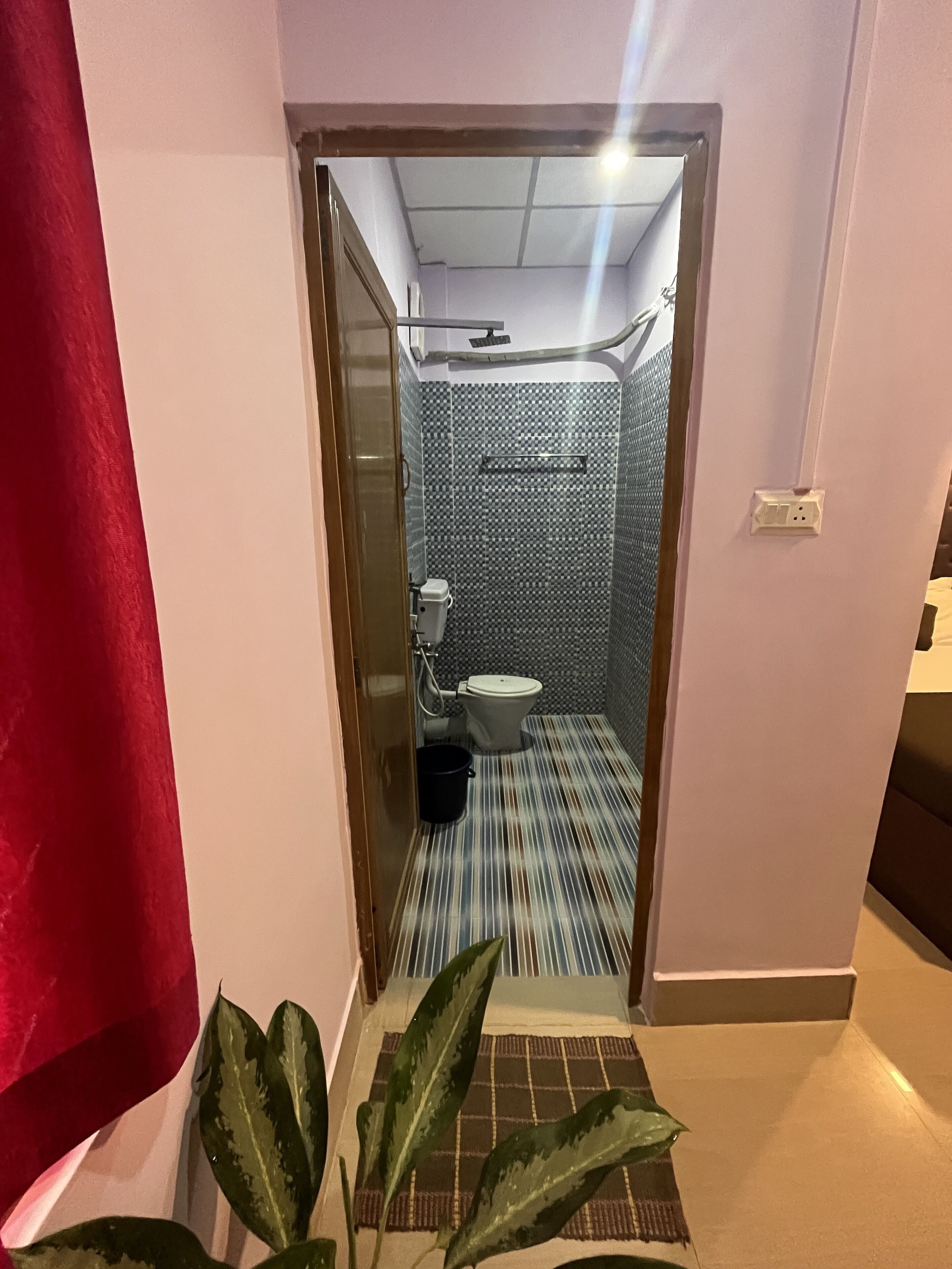 A narrow hallway leading to a bathroom with a striped floor, a toilet, and a shower area.