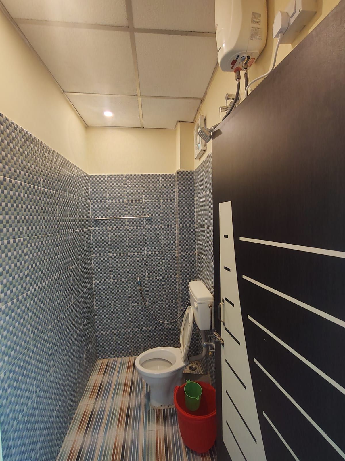 A bathroom with a tiled shower wall, a toilet, and a striped floor.