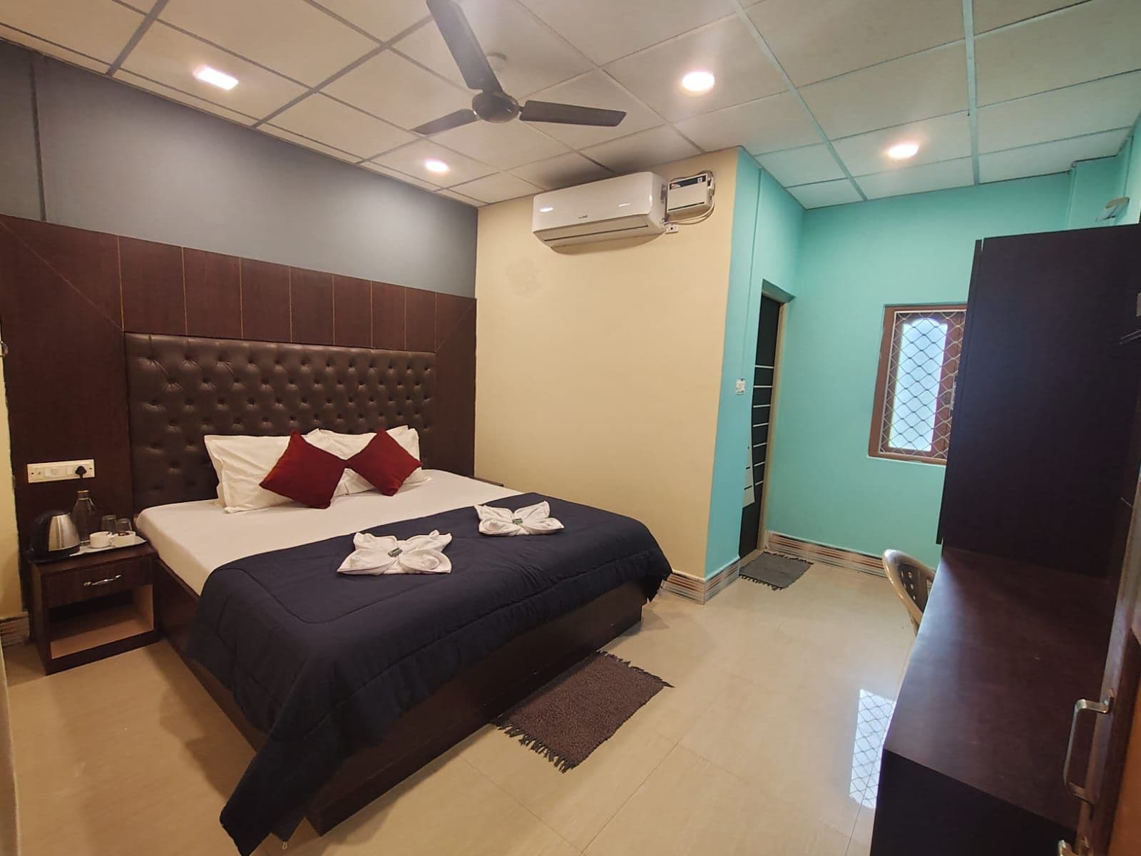 Ein Hotelzimmer mit Bett, Deckenventilator, Klimaanlage, Schreibtisch und Kleiderschrank.