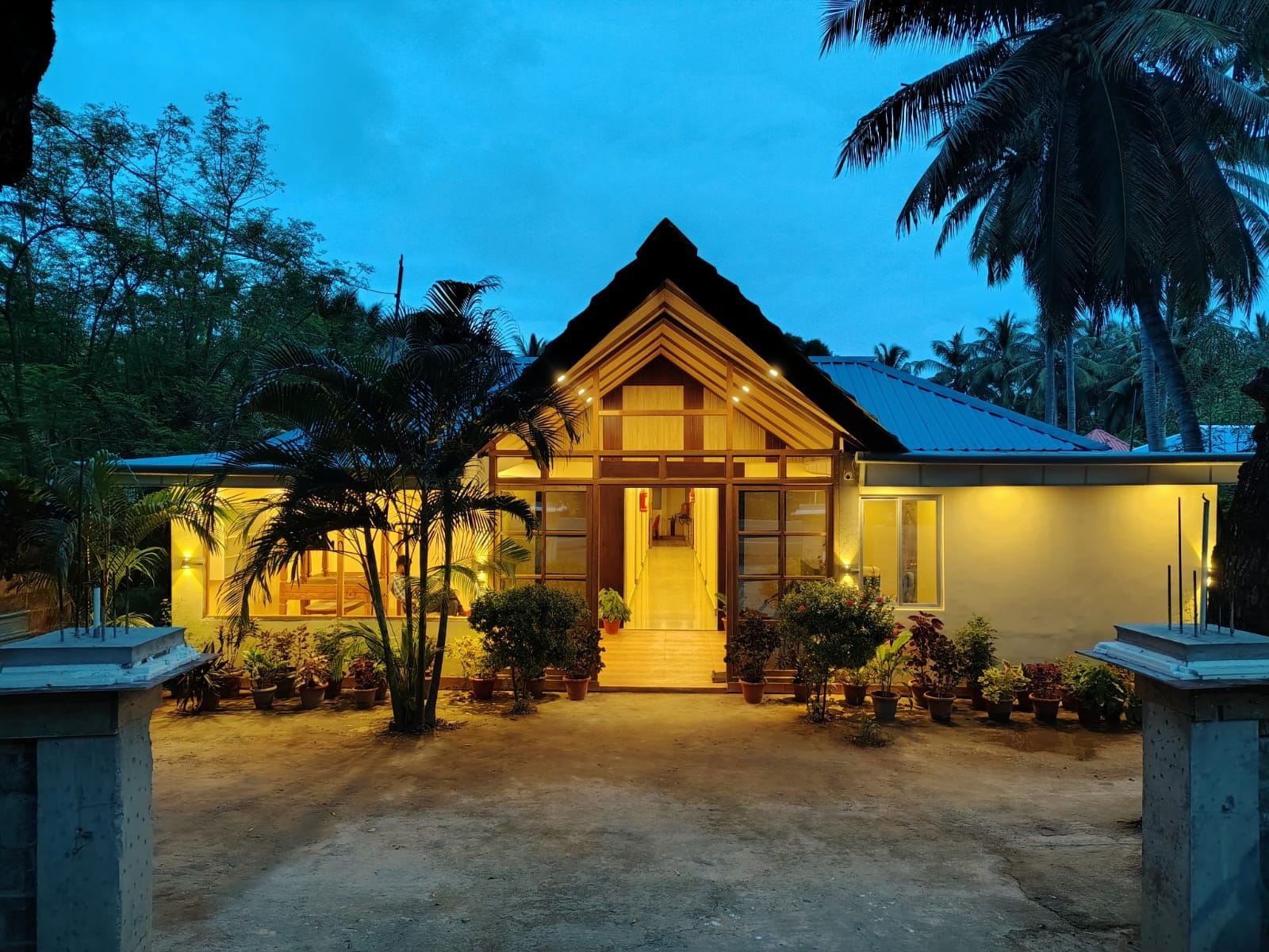 A two-story house with a pitched roof, surrounded by potted plants and palm trees.