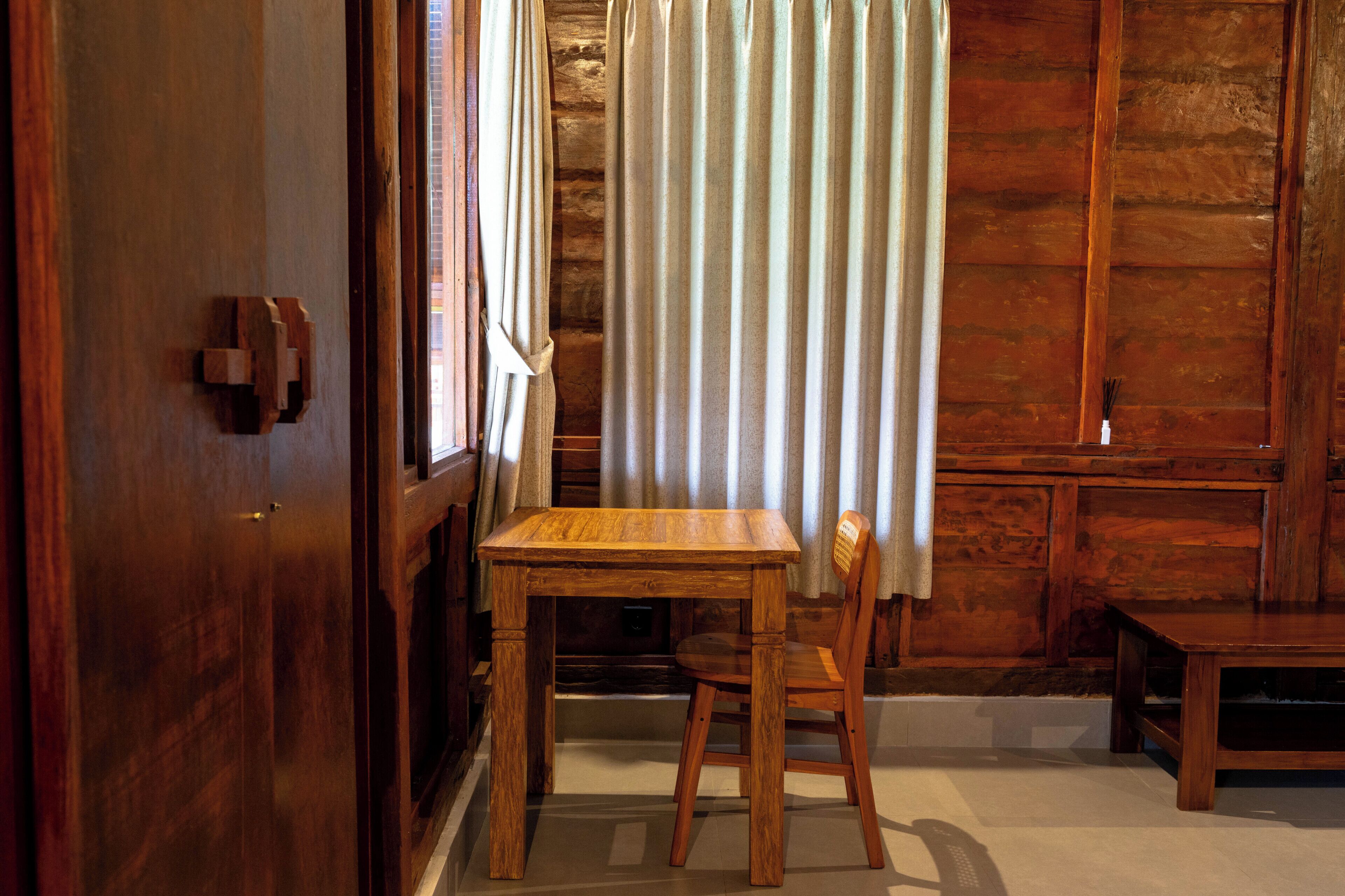 A wooden interior with a table and chair, a wooden door, and a curtain.