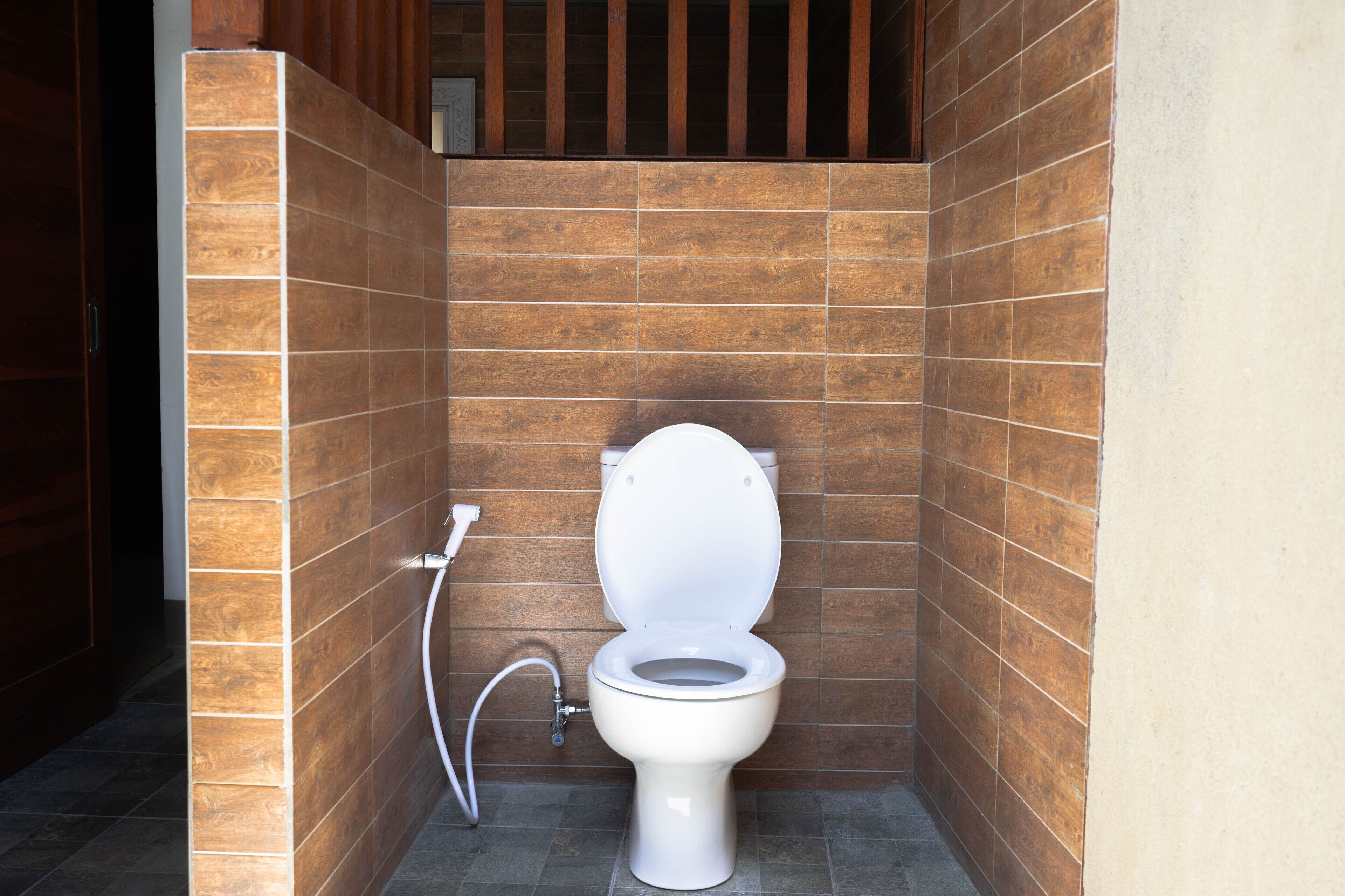 A small, enclosed bathroom with a toilet, a handwashing station, and wooden paneling on the walls.