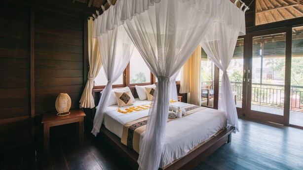 Ein Schlafzimmer mit einem Himmelbett, Holzwänden, einer Bank und Blick ins Freie.