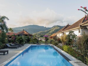 Une piscine entourée de chaises longues, de plantes tropicales et d’une architecture traditionnelle.