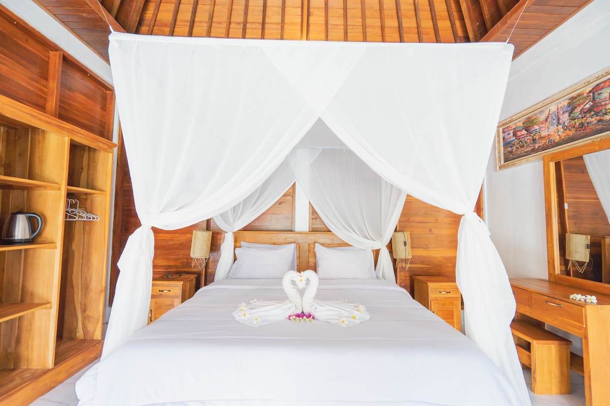 Une chambre avec un lit, une tête de lit en bois, un baldaquin blanc et un cygne décoratif fait de serviettes.
