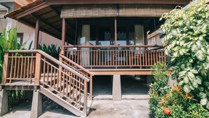 Ein traditionelles Holzhaus mit Balkon, Betontreppen und üppiger Bepflanzung.