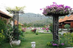 Un jardin agrémenté d’une pergola, d’une colonne en pierre et d’un sentier menant à un bâtiment surmonté d’un toit en tuiles.