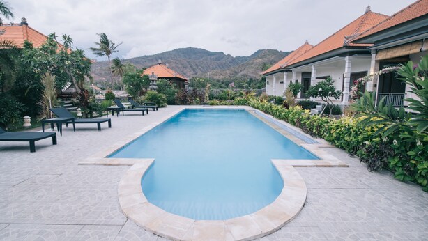 A swimming pool with lounge chairs, surrounded by greenery and buildings with red-tiled roofs.