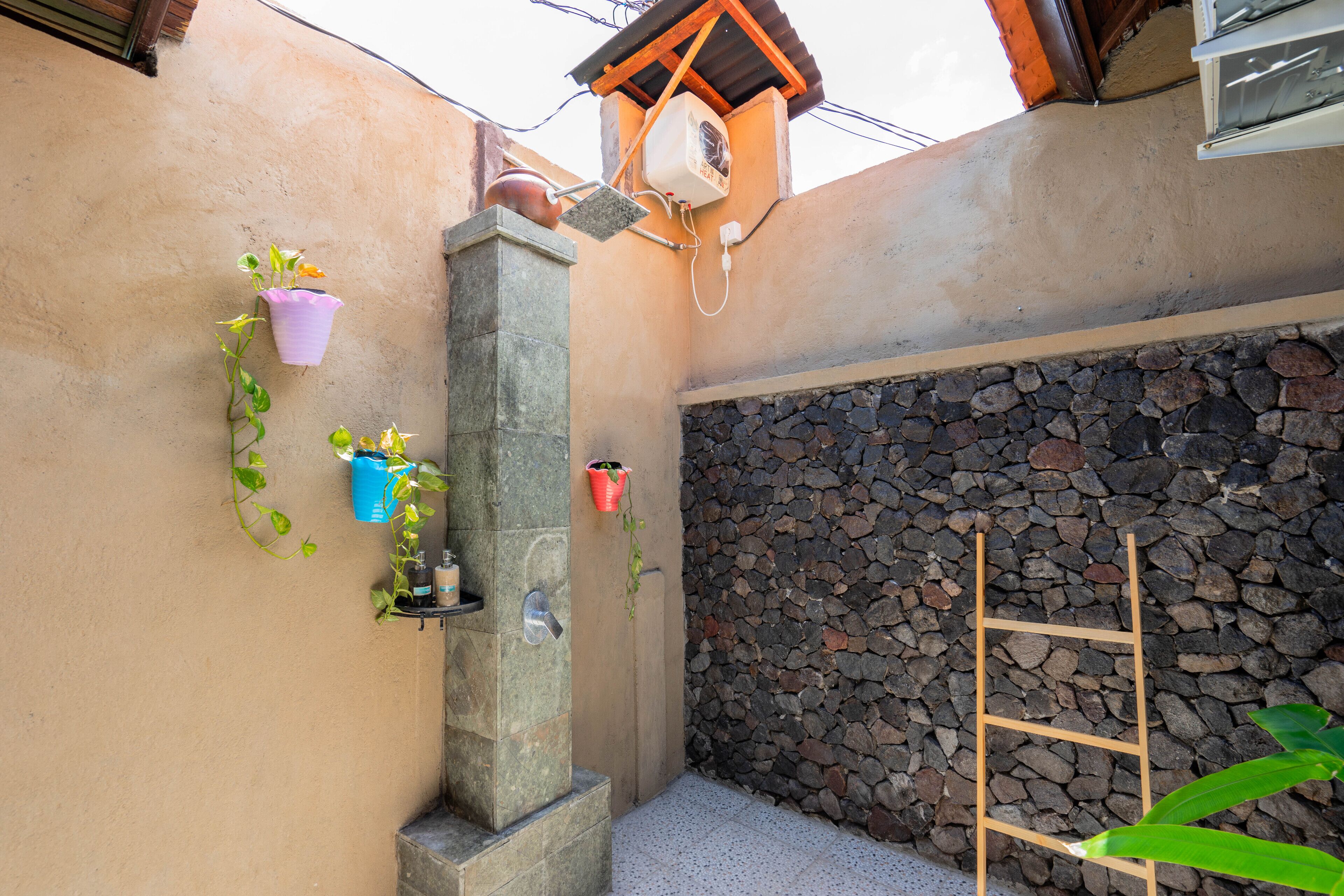 Un muro de piedra con una escalera de madera, una estructura de hormigón y plantas en macetas.