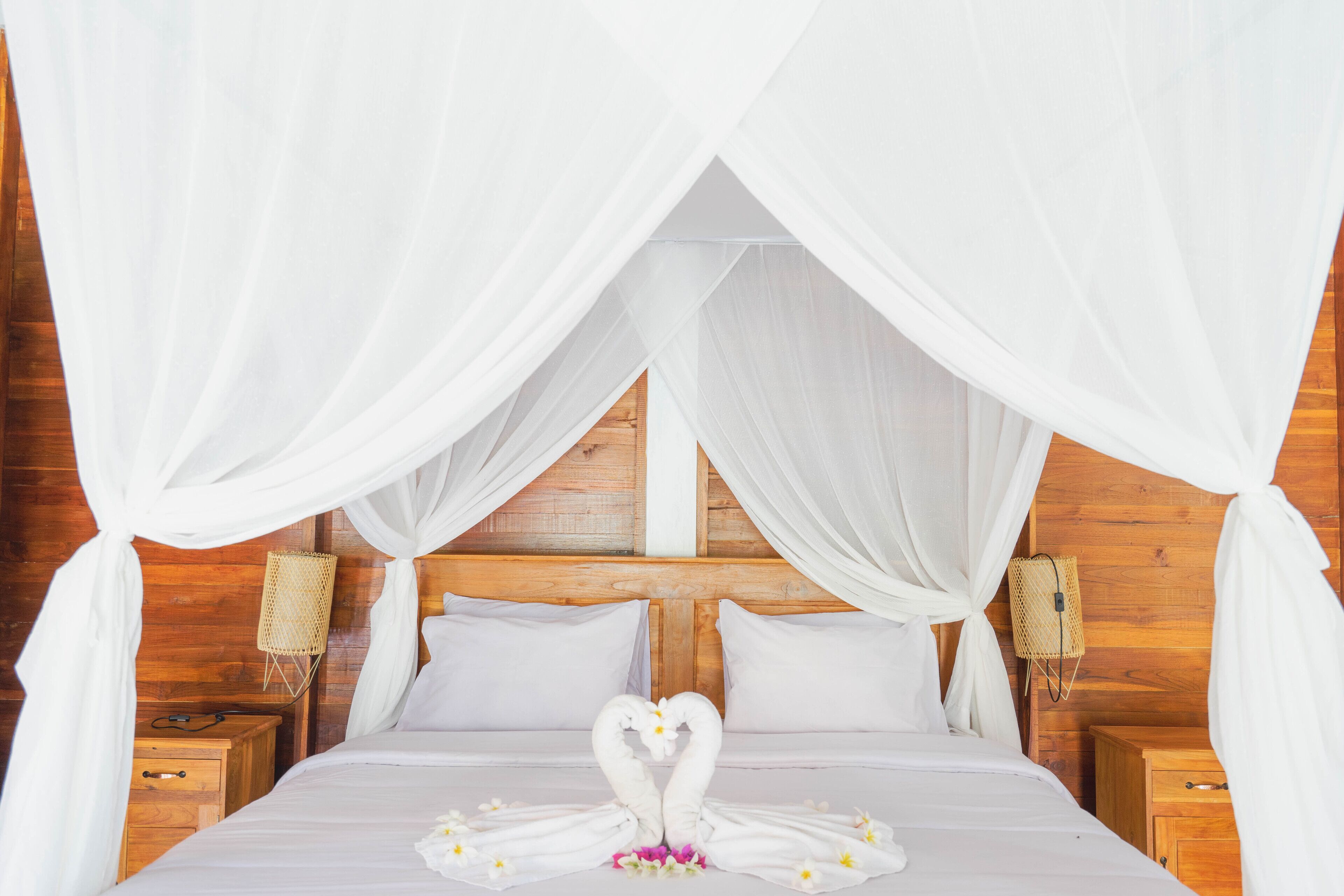 A bed with white bedding and a canopy, a wooden headboard, and two bedside tables with lamps.
