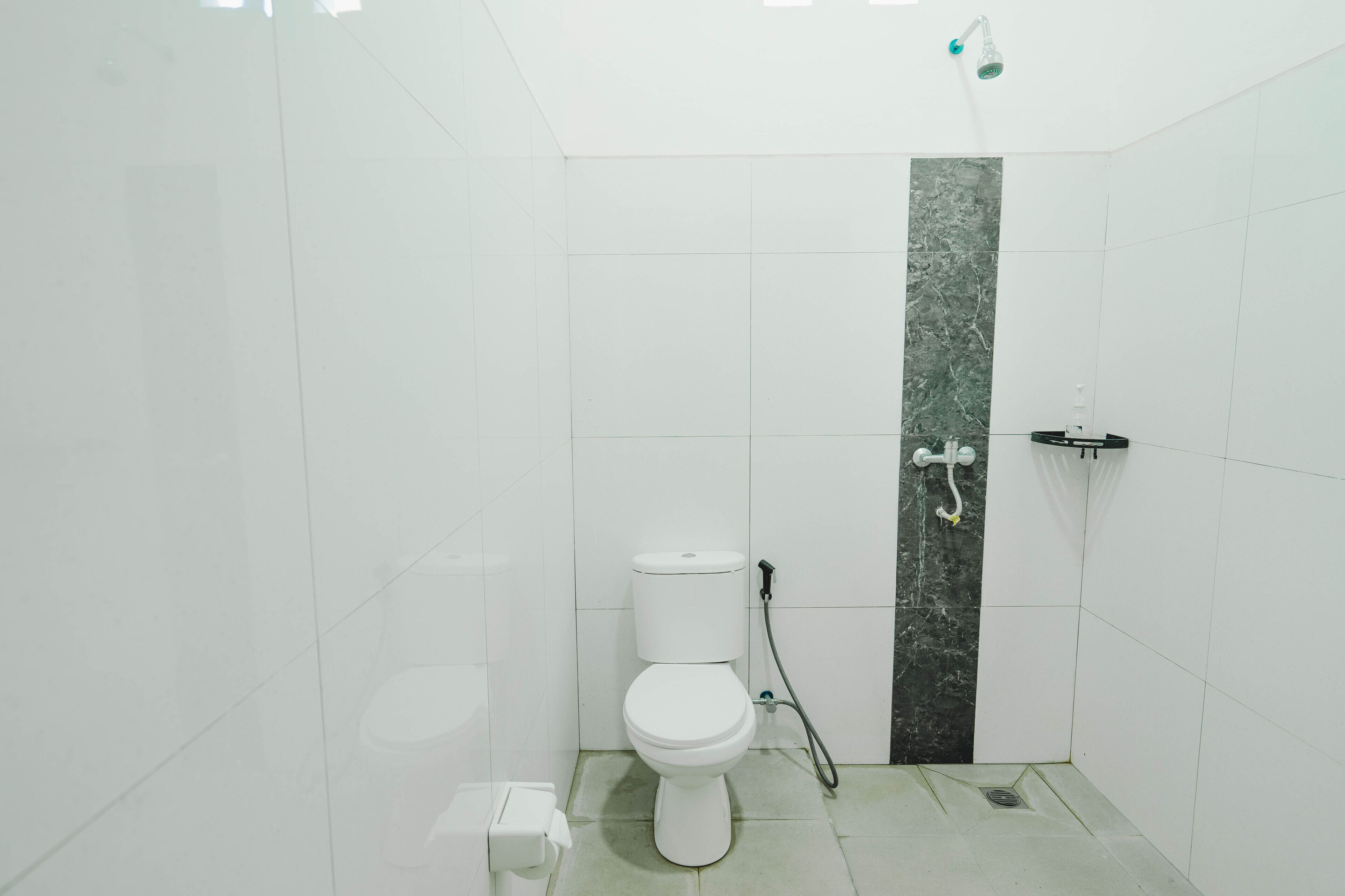 A small, modern bathroom with white tiles, a white toilet, a shower with a handheld showerhead, and a marble accent wall.