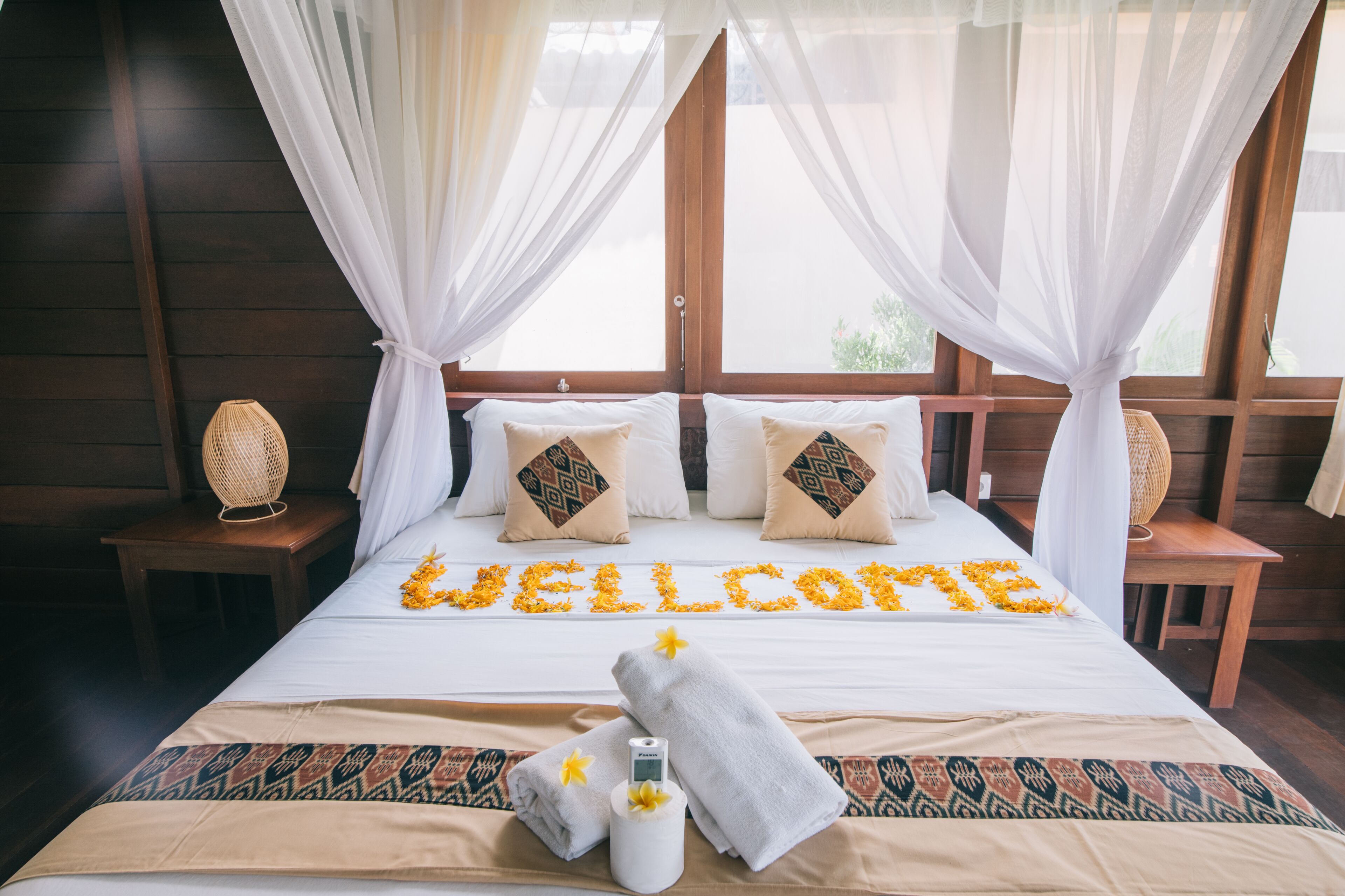 Una cama con un letrero de flores que dice 'WELCOME', una botella y toallas.