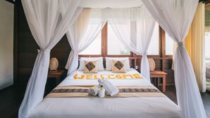 A bed with a canopy, a welcome mat, and a towel on the bed.