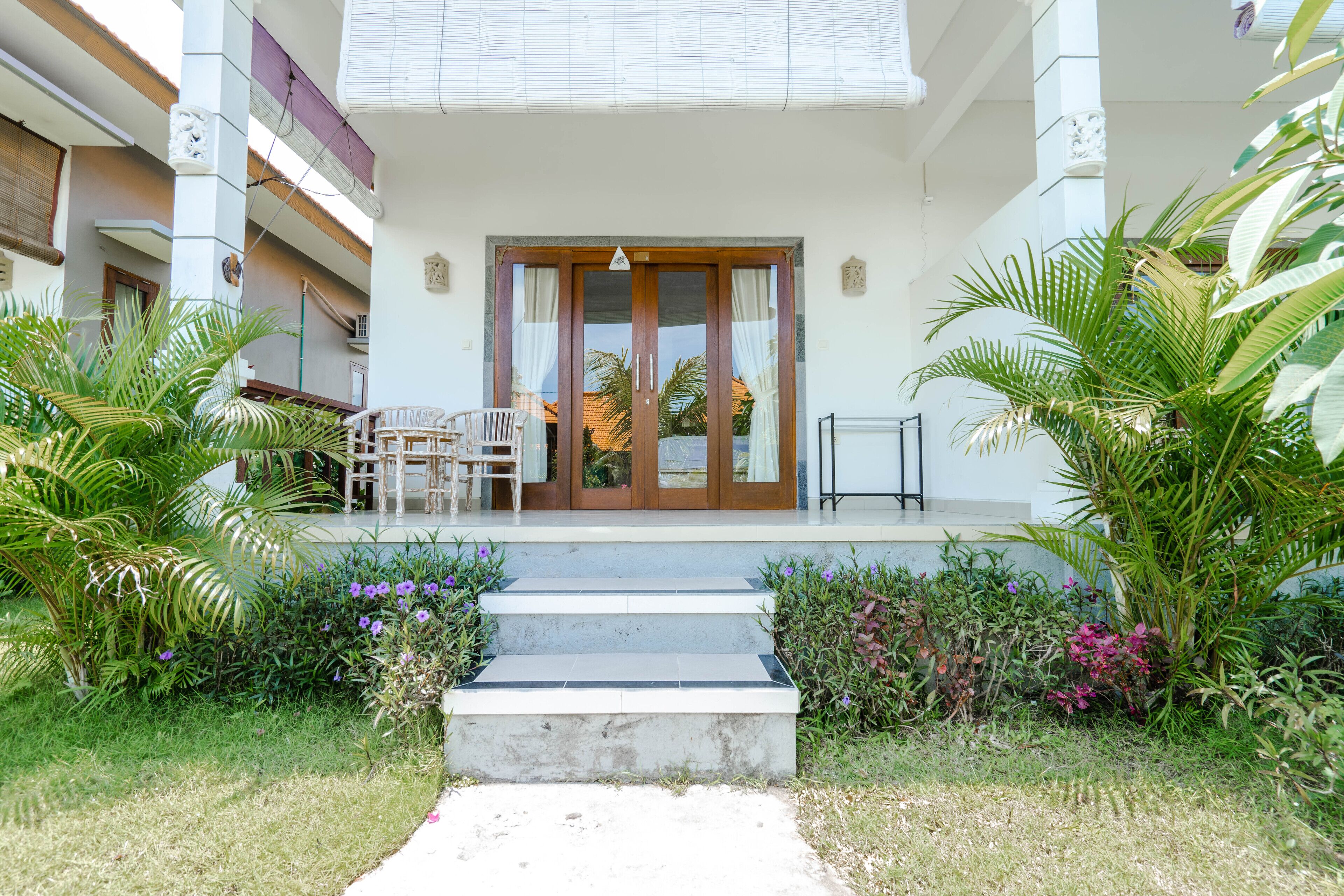 A hotel entrance with a covered porch, a staircase, and a seating area with chairs.