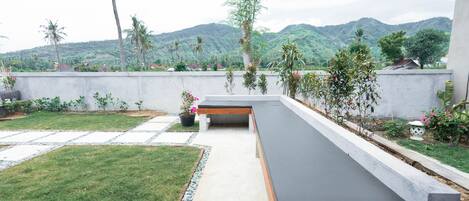 A modern outdoor seating area with a concrete pathway, surrounded by potted plants and a view of lush green hills.