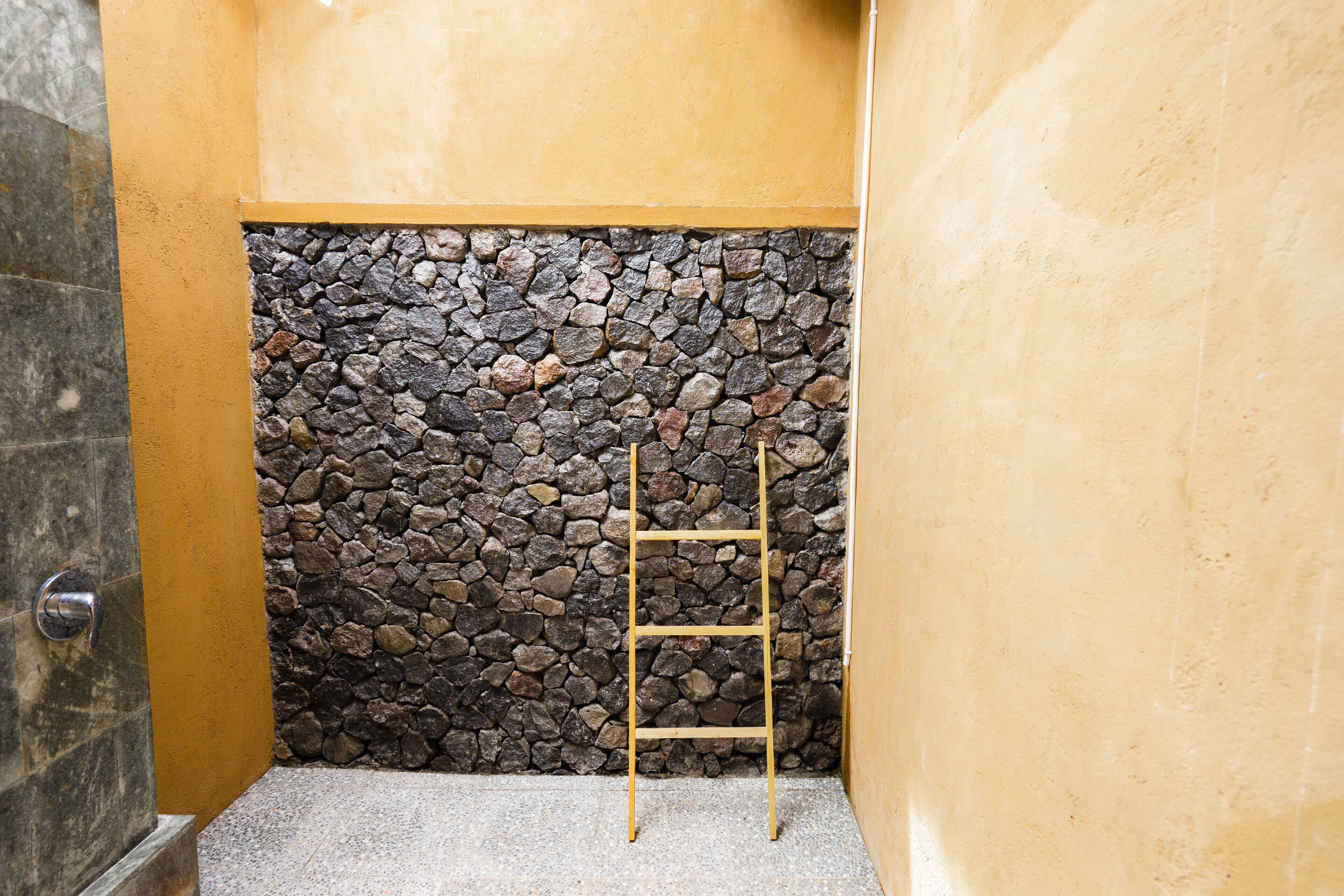Un baño con pared de piedra, una escalera de madera y una puerta.