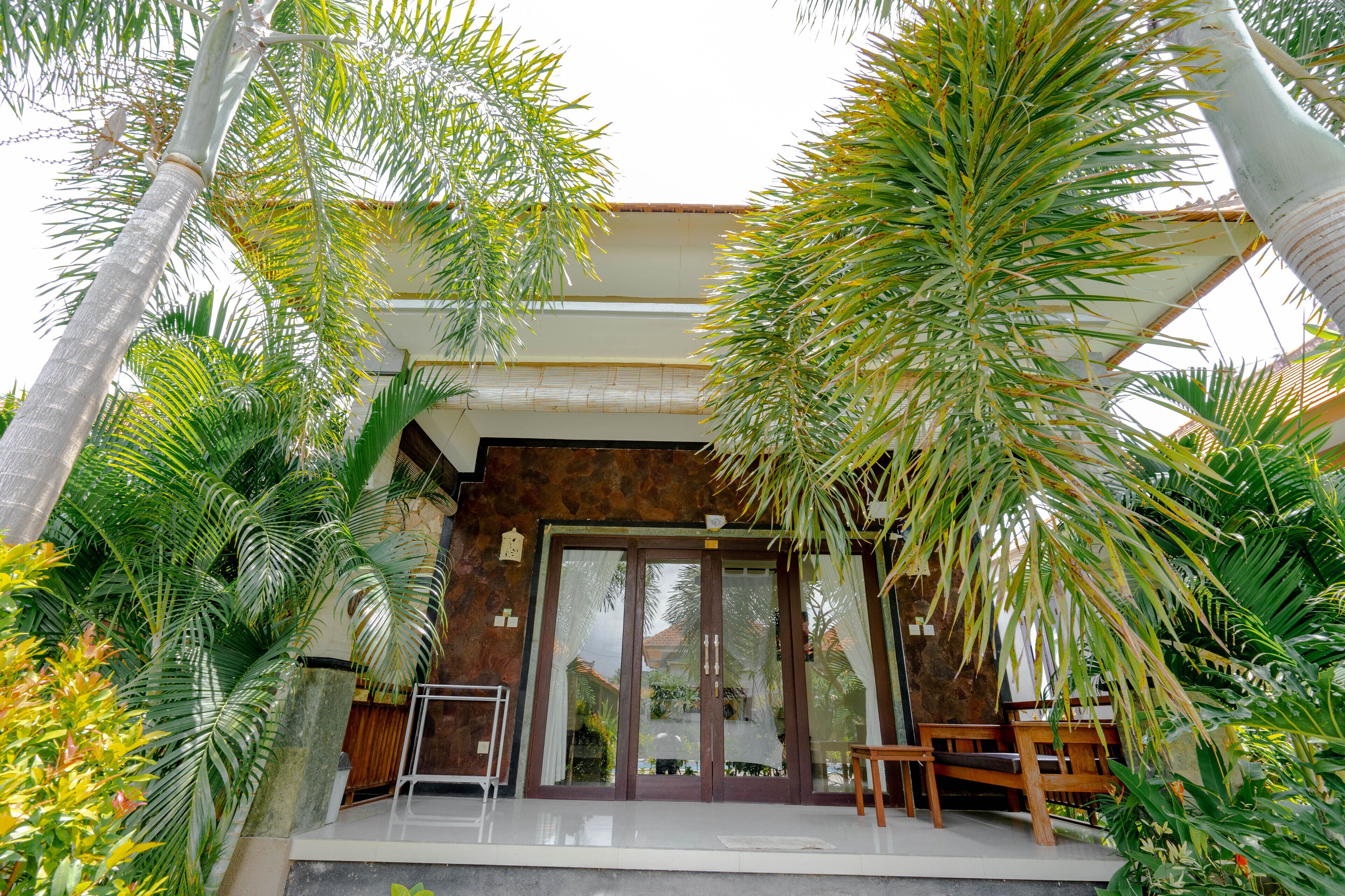 A modern building with a glass door entrance, surrounded by lush tropical plants.