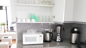 Una cocina moderna con armarios blancos, un microondas, una cafetera y diversos utensilios de cocina.