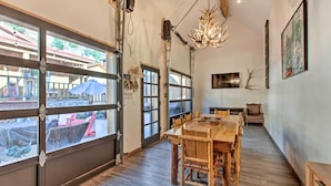 Un comedor espacioso con una gran mesa de madera y sillas, ventanas amplias con vistas al exterior y una araña.