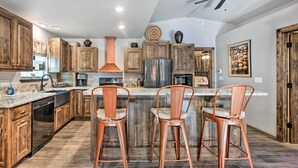 Una cocina con armarios de madera, un refrigerador de acero inoxidable y una barra con dos taburetes.
