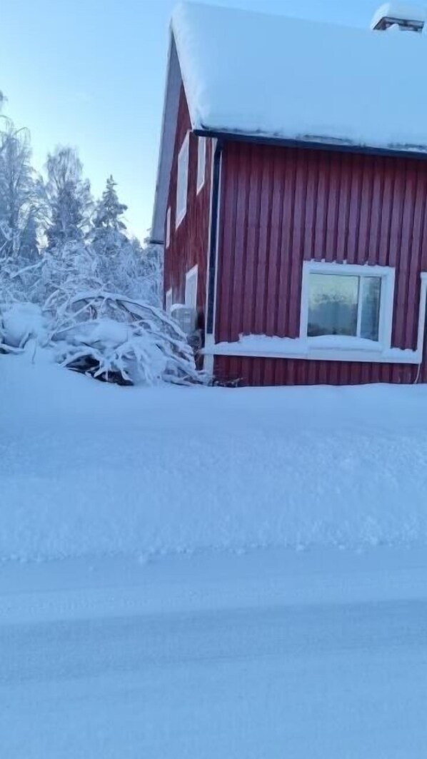 A red wooden building with a snow-covered roof and a window.