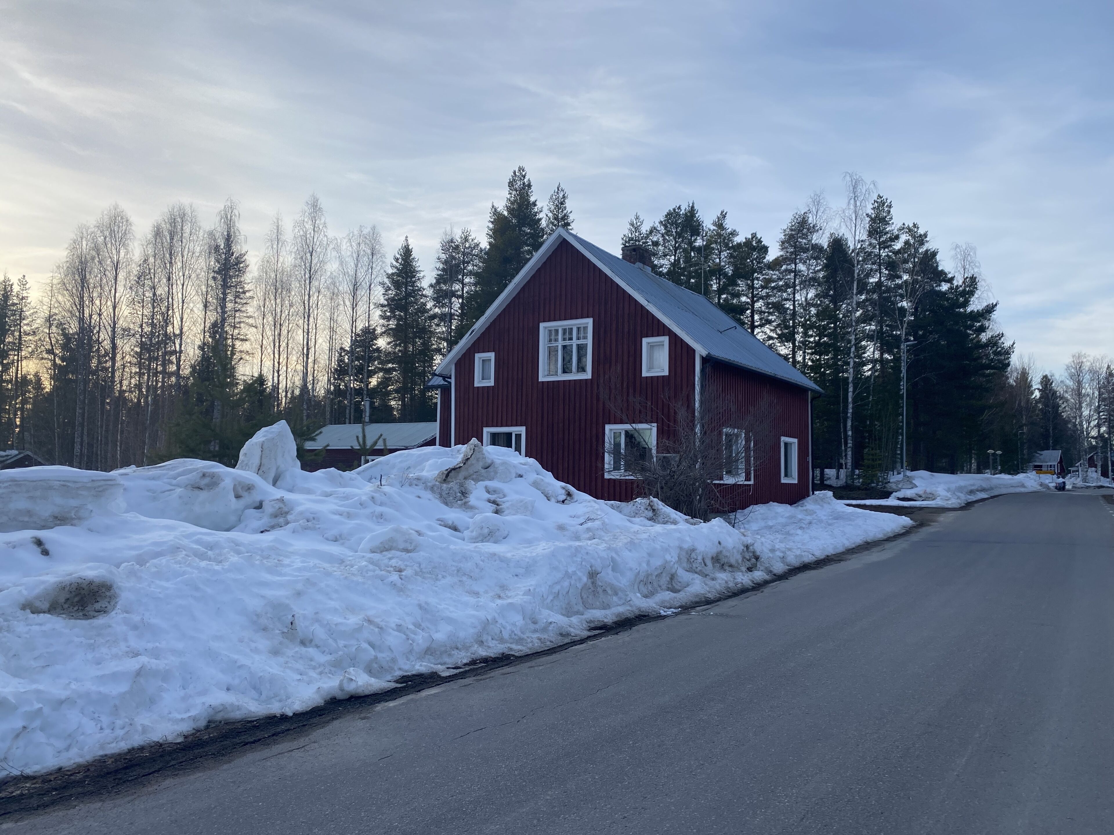 Et rødt træhus med skråt tag, omgivet af sne og træer.