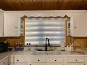 A kitchen with white cabinets, a black faucet, and a window with blinds. - Enjoy Springtime at Bryce’s Zion House by Zion and Bryce National Parks! (Panguitch)