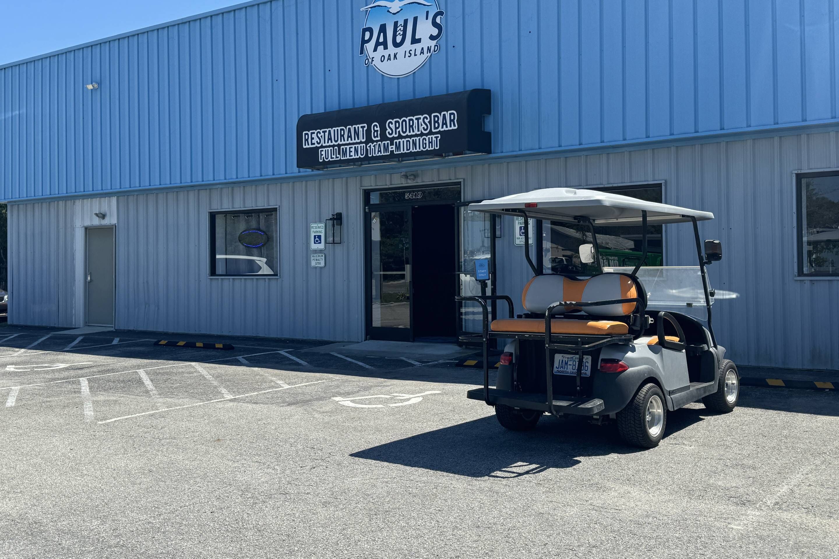 Un bâtiment sur lequel on peut lire l’enseigne « Paul’s Restaurant & Sports Bar », avec un véhicule de golf garé devant.
