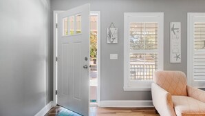 Un pasillo con una puerta blanca, una ventana con persianas y un cuadro con una cita en la pared.