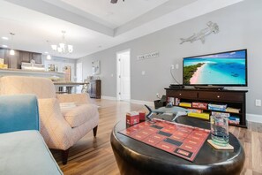 A living room with a television displaying a beach scene, a board game, and a shark figurine. - Great For Family Vacation,Golf Cart Included (Oak Island)