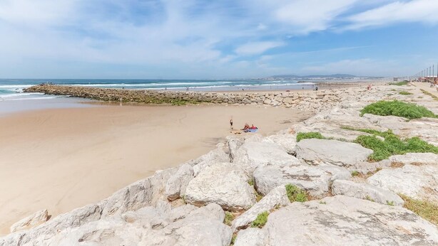 Una playa con costa rocosa, arena y cielo despejado.
