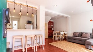 Una sala de estar moderna con un sofá, un comedor con mesa y sillas, y una cocina con mostrador y taburetes.