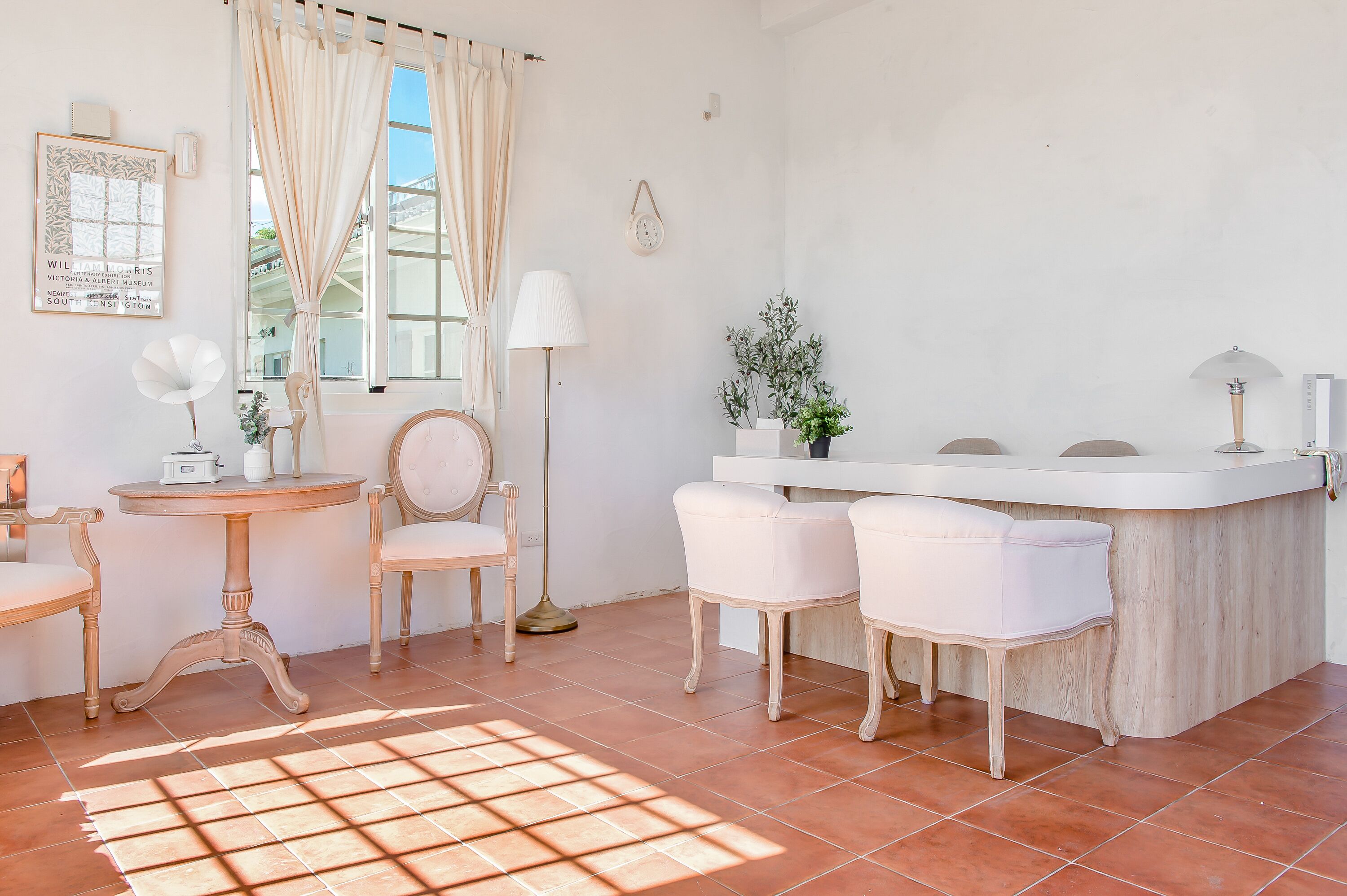 A bright, well-lit room with a white vanity, two white chairs, a round table, and a floor lamp.
