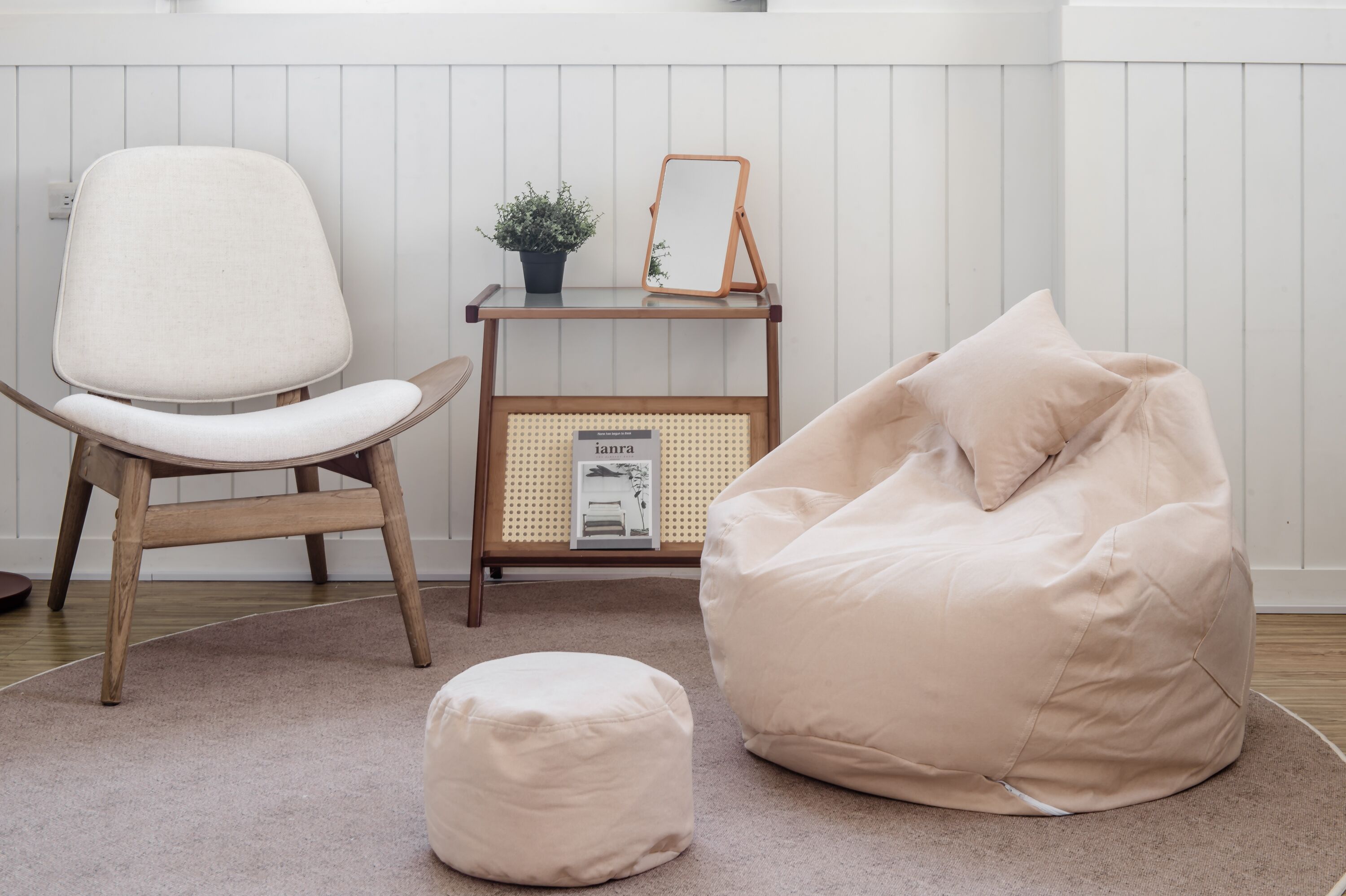 A room with a wooden chair, a bean bag, and a small table with a plant and a mirror.