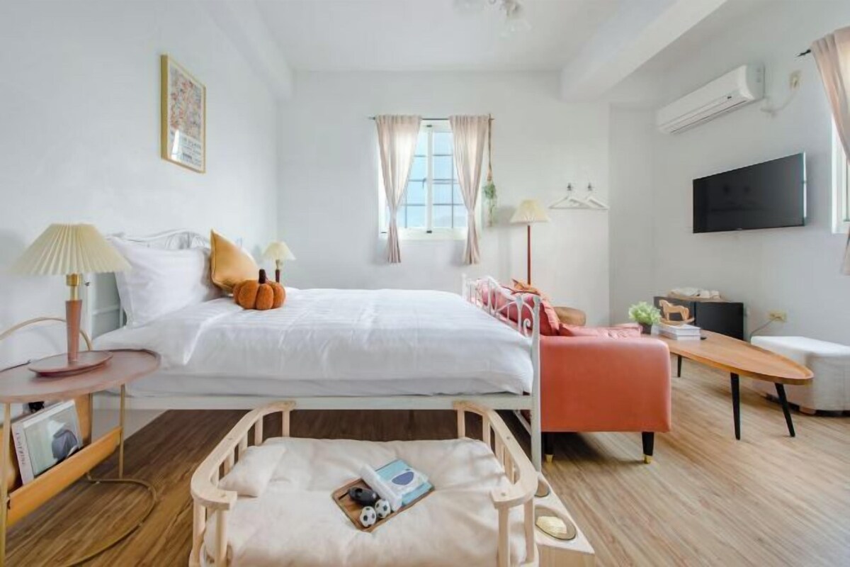 Quarto de hotel com cama, mesas de cabeceira, escrivaninha, cadeira, televisão e janela com cortinas.