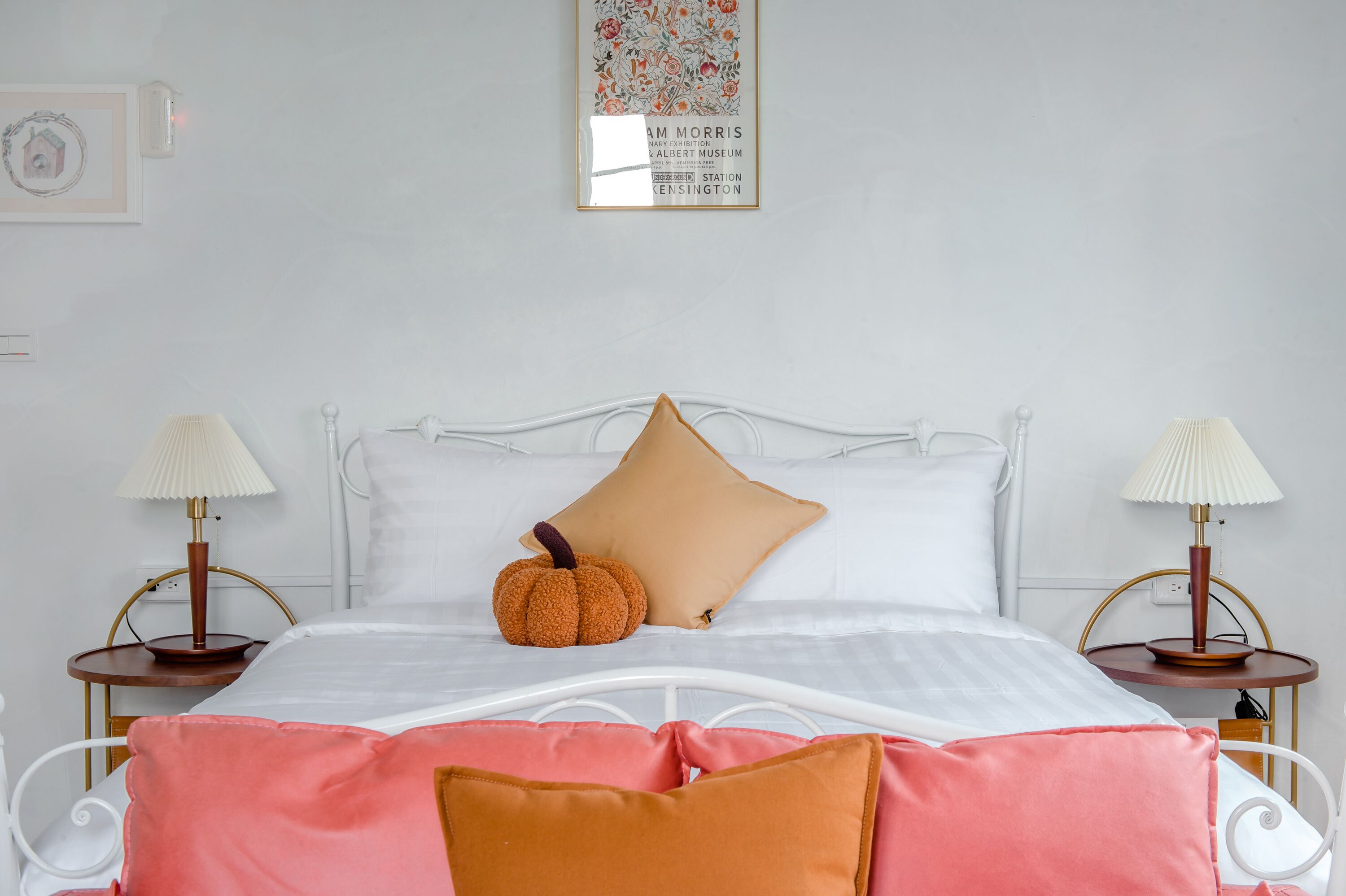 A neatly made bed with white linens, a brown pillow, and a small orange pumpkin decoration. There are two bedside tables with lamps, and a framed picture on the wall.