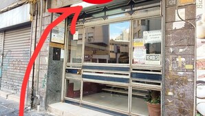 Une devanture de magasin avec un volet métallique, une enseigne portant le numéro 121 et une flèche rouge pointant vers le volet.