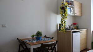 Une cuisine compacte équipée d’un four à micro-ondes, d’un petit réfrigérateur et d’un meuble en bois. On y trouve une table à manger avec des chaises, ainsi qu’une petite plante en pot posée dessus.