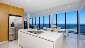 Een moderne keuken met een groot eiland, roestvrijstalen apparatuur en uitzicht op de oceaan.