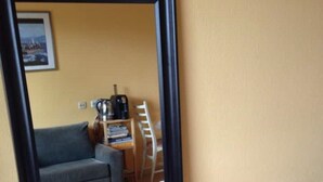 Une pièce avec un grand miroir, un canapé gris, une petite table avec une machine à café et un meuble blanc.