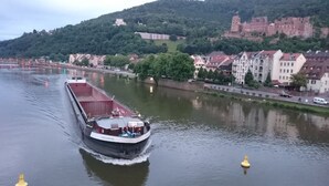 Un bateau fluvial navigue sur une rivière, avec des bâtiments et un château en arrière-plan.