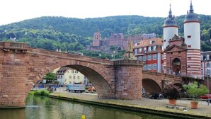 Un pont de pierre enjambant une rivière, avec des bâtiments et une colline en arrière-plan.