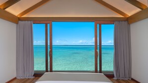 Une chambre avec une grande fenêtre, des poutres apparentes en bois au plafond et un lit.