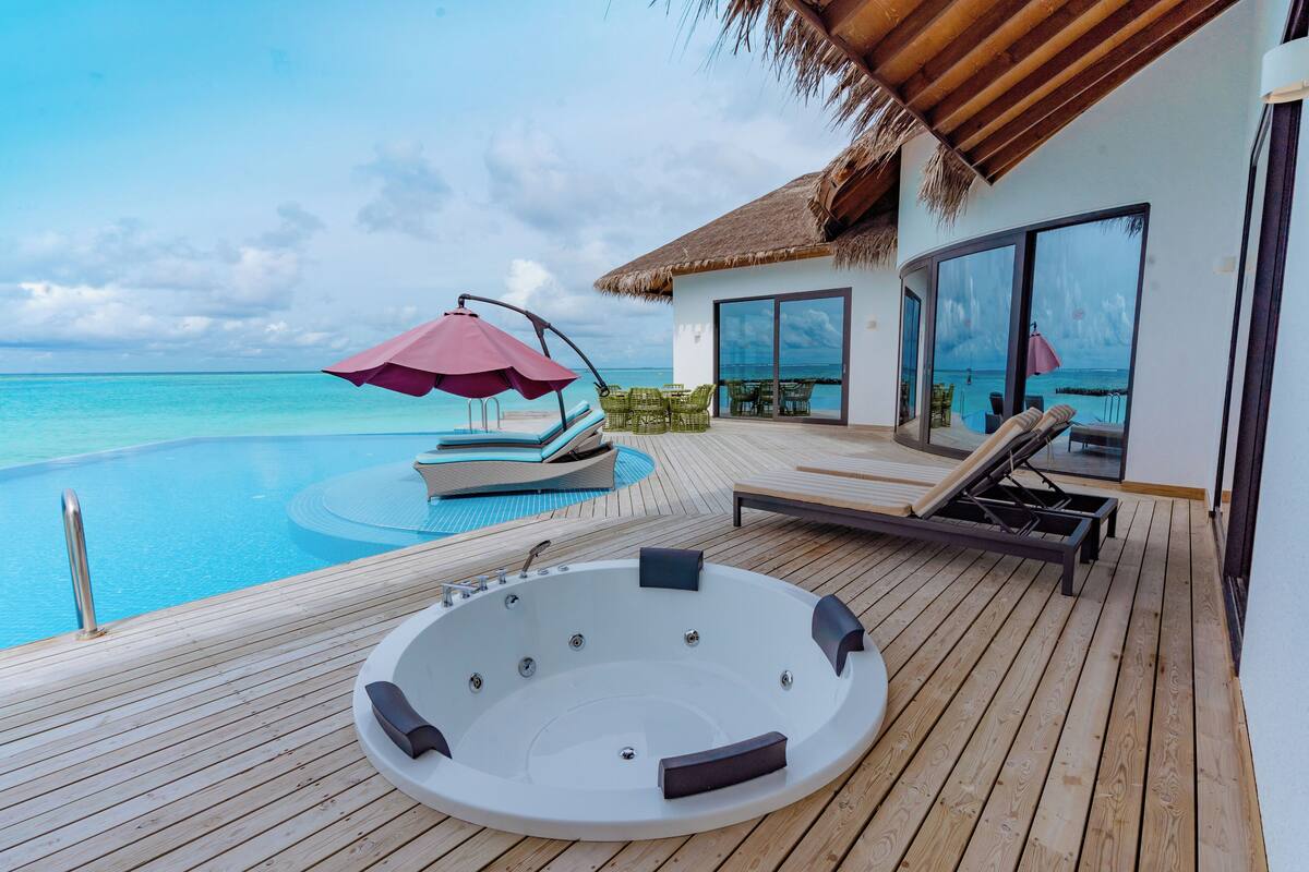 Una terraza de madera con un jacuzzi, sillas de descanso y una piscina con vista al océano.
