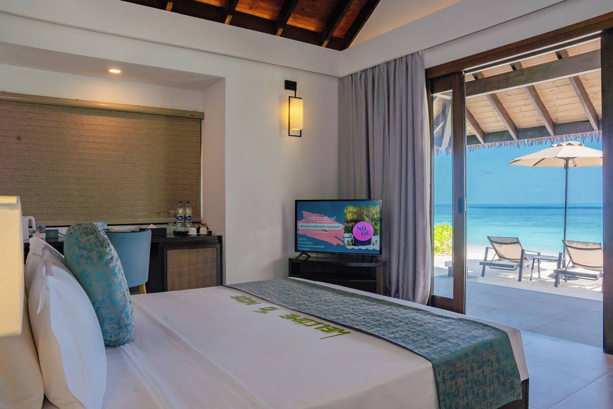 Una habitación de hotel con cama, escritorio, televisión y vista a la playa.